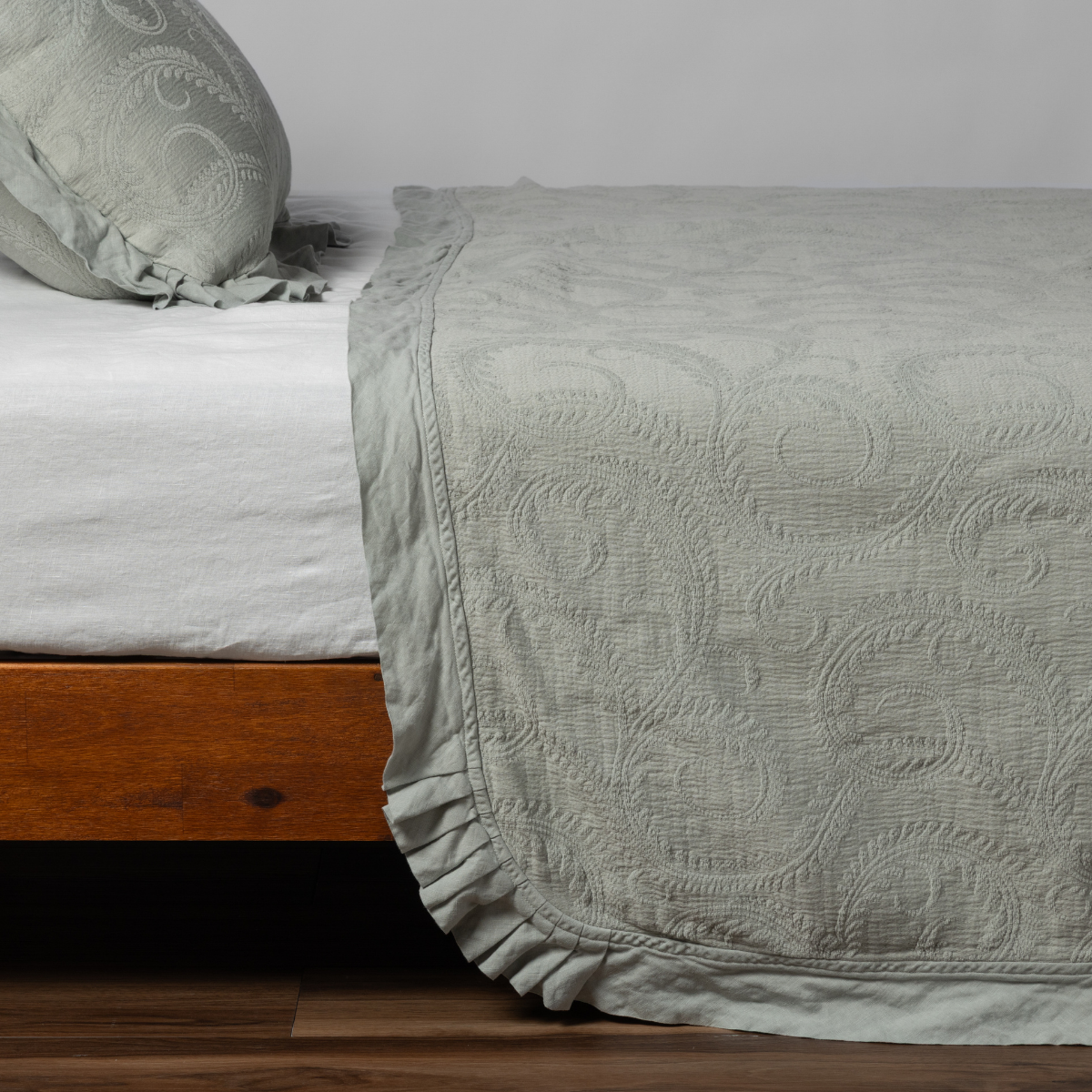 Eucalyptus matelassé bedspread with ruffled hem draping over bed corner, paisley quilt pattern.