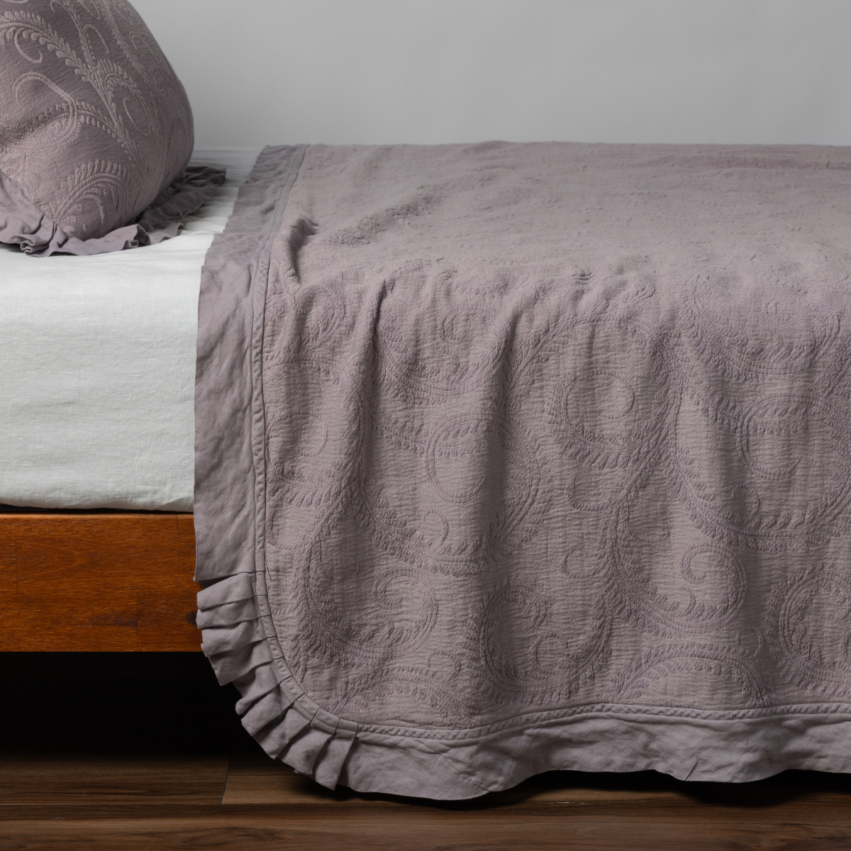 French Lavender bedspread with ruffled hem and tonal scrolling pattern draped over bed corner.