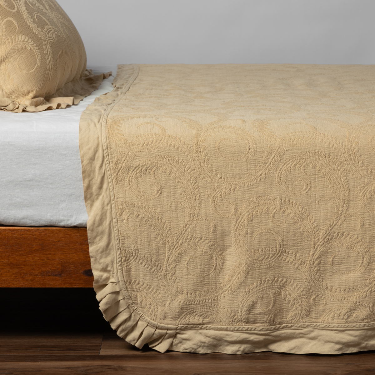 Honeycomb matelassé bedspread with scrollwork pattern and ruffled hem, draped over bed foot.