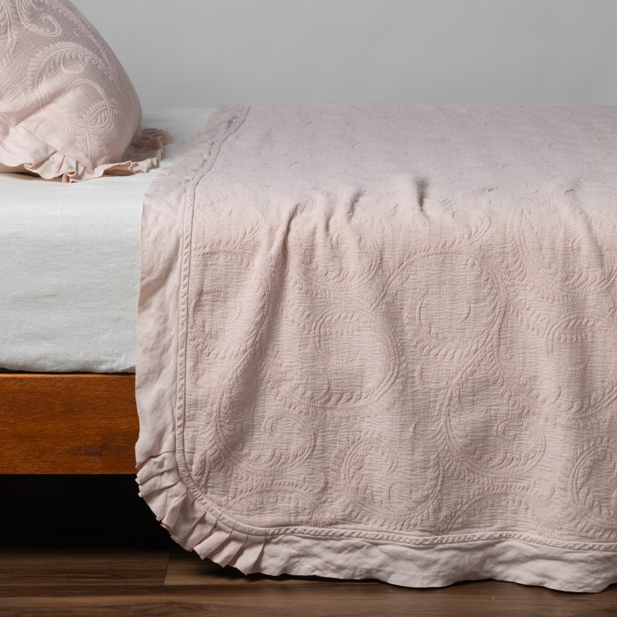 Pearl Bella Notte Marisette bedspread with scrollwork quilting and ruffled hem draped over bed.