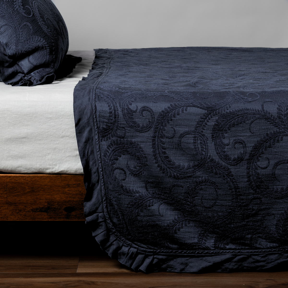 Slate Marisette bedspread corner showing scrollwork quilting and ruffle trim detail.