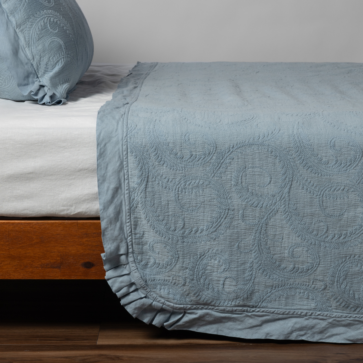 Marisette bedspread corner detail showing quilted scroll pattern in Tahoe Blue on wooden bed frame.