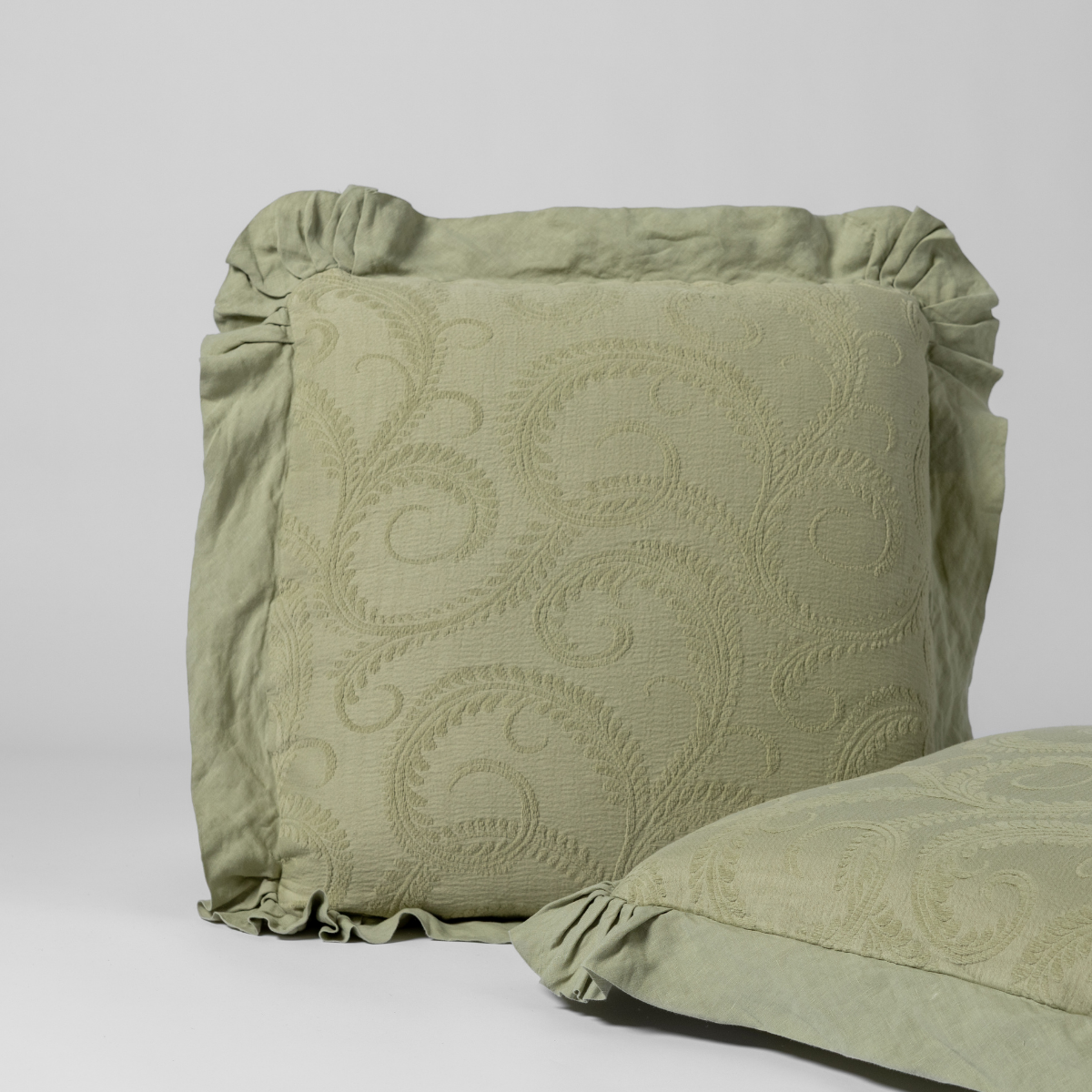 Desert Sage sham with tone-on-tone scrolling embroidery and gathered ruffle trim, angled view.