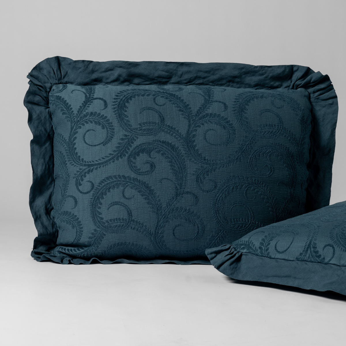 Midnight Marisette sham with tone-on-tone scroll embroidery and ruffled border, angled view.