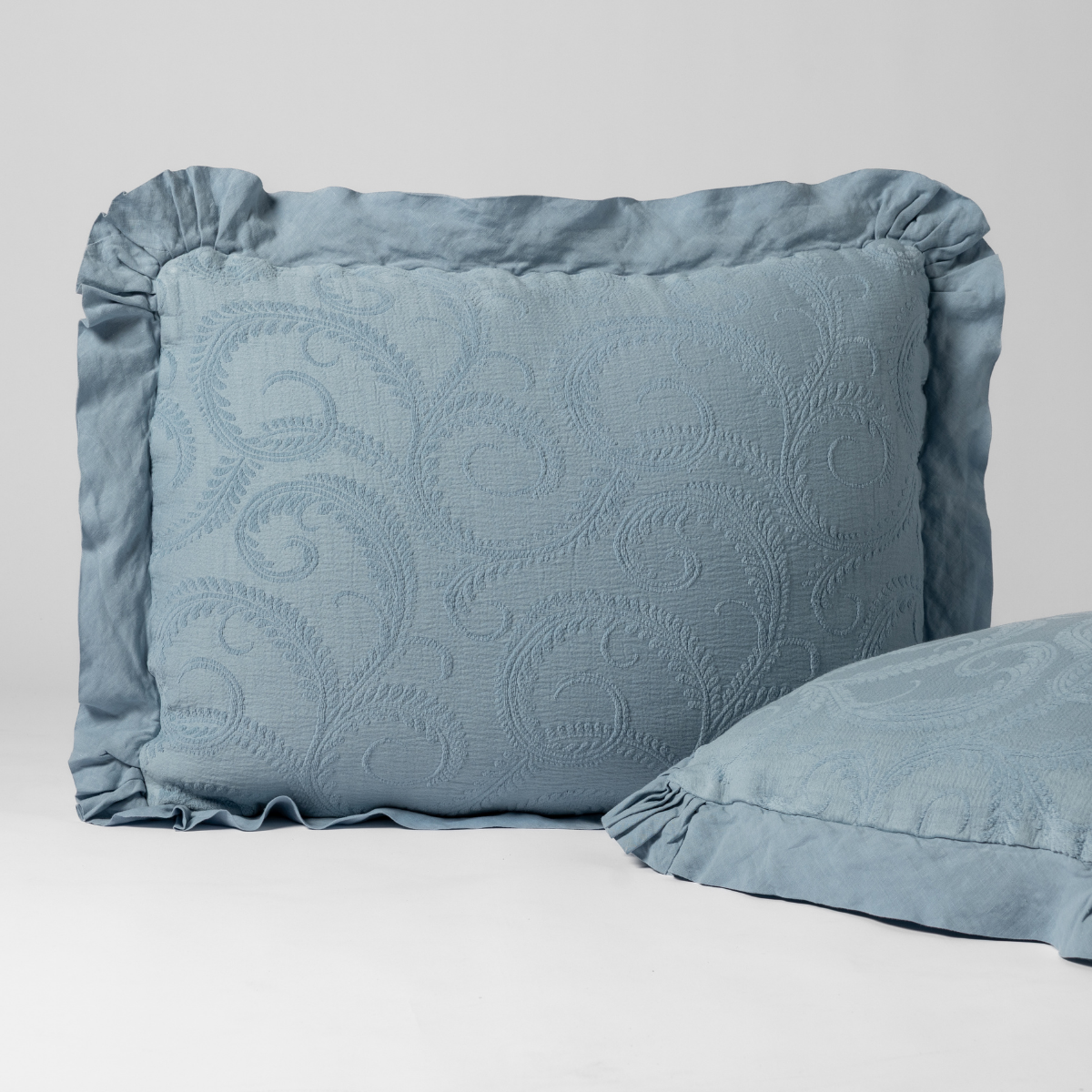 Marisette sham in Tahoe Blue, ruffled border with tonal scroll matelassé, second sham partially visible.