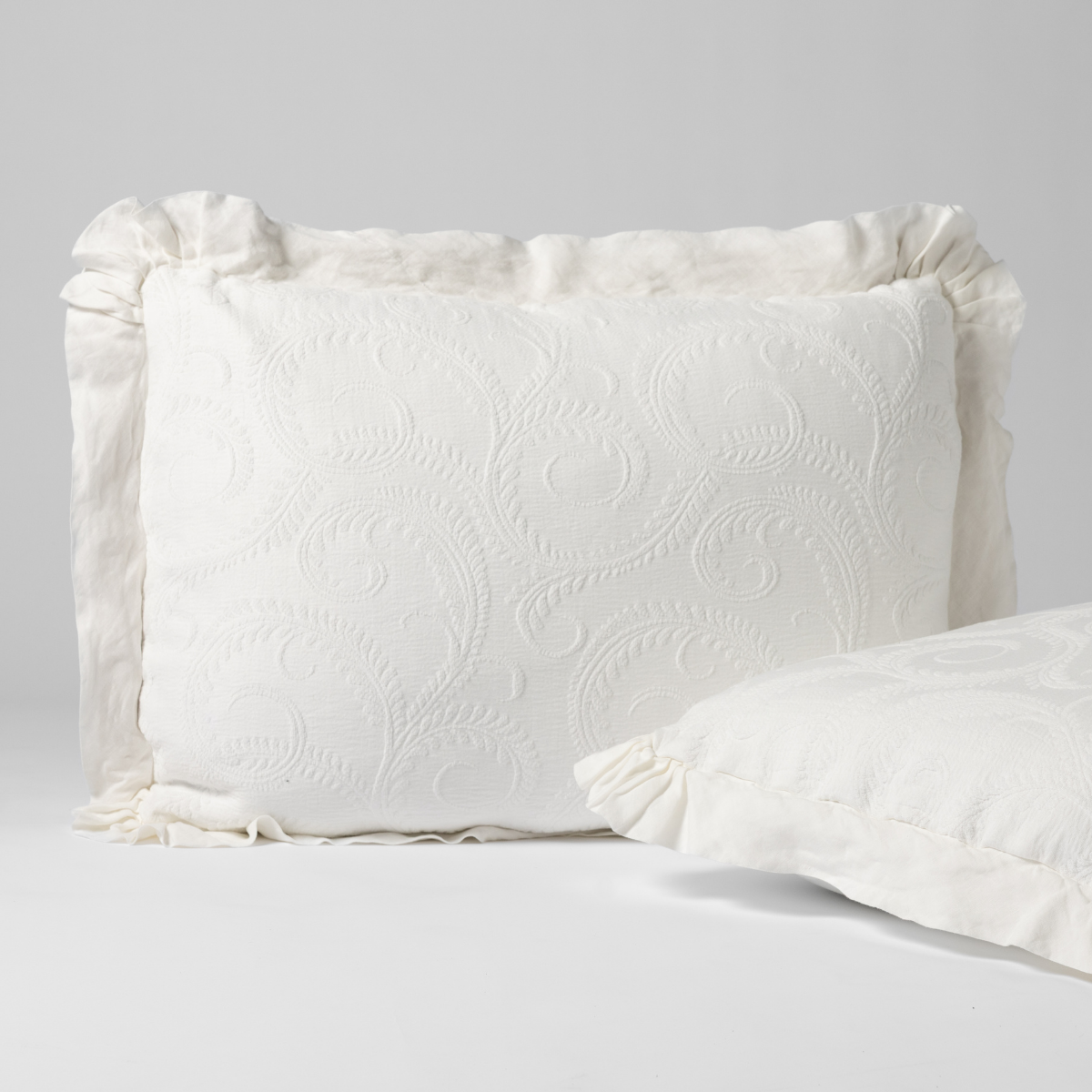 Close-up of Bella Notte Marisette sham in Winter White with embossed floral scrollwork and ruffled linen trim.