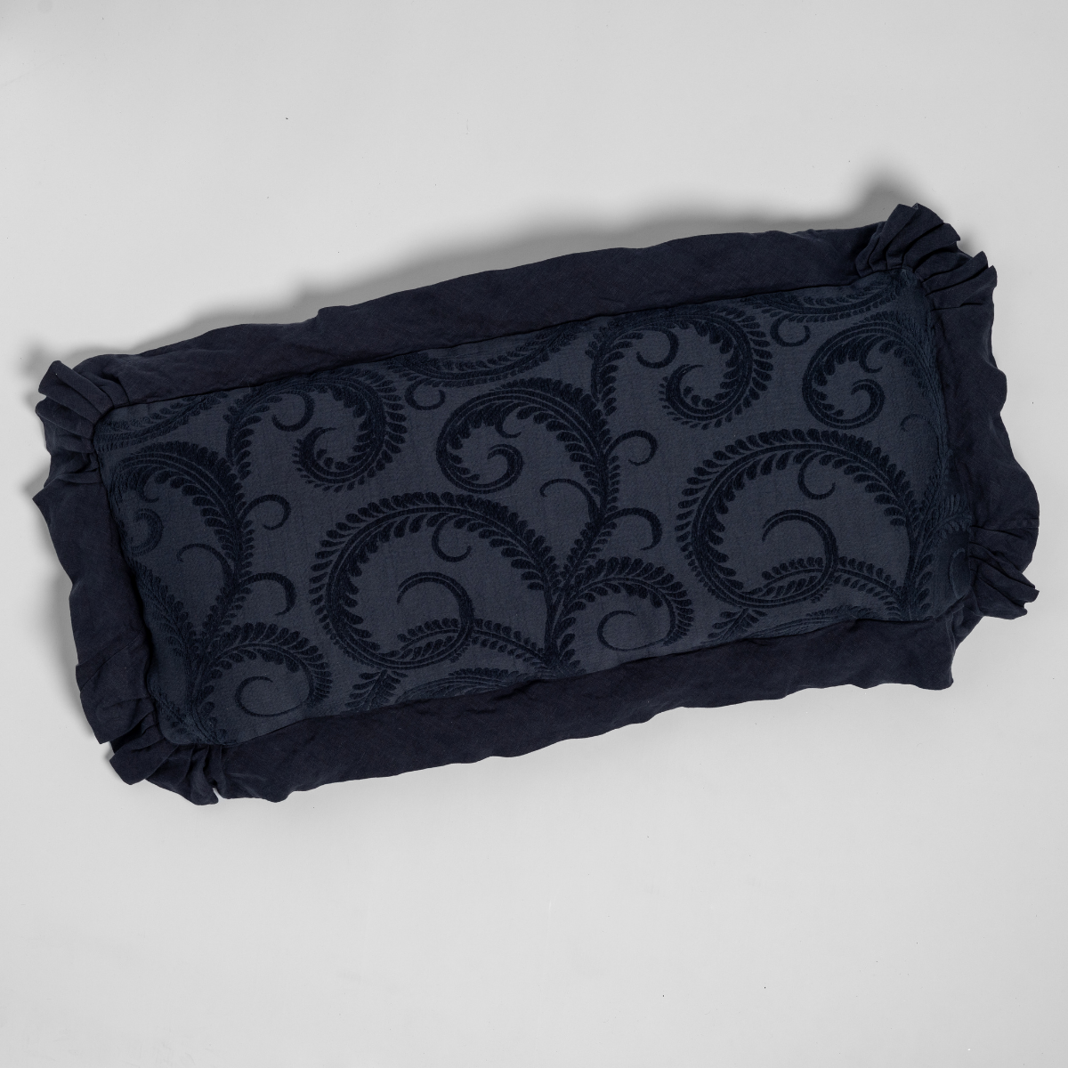 Slate embroidered scrollwork on throw pillow with ruffled border, flat lay view.