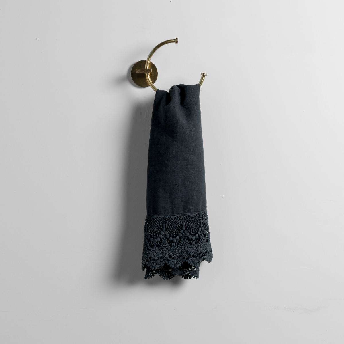 Slate guest towel with crochet lace hem, hung folded on a brass wall hook.