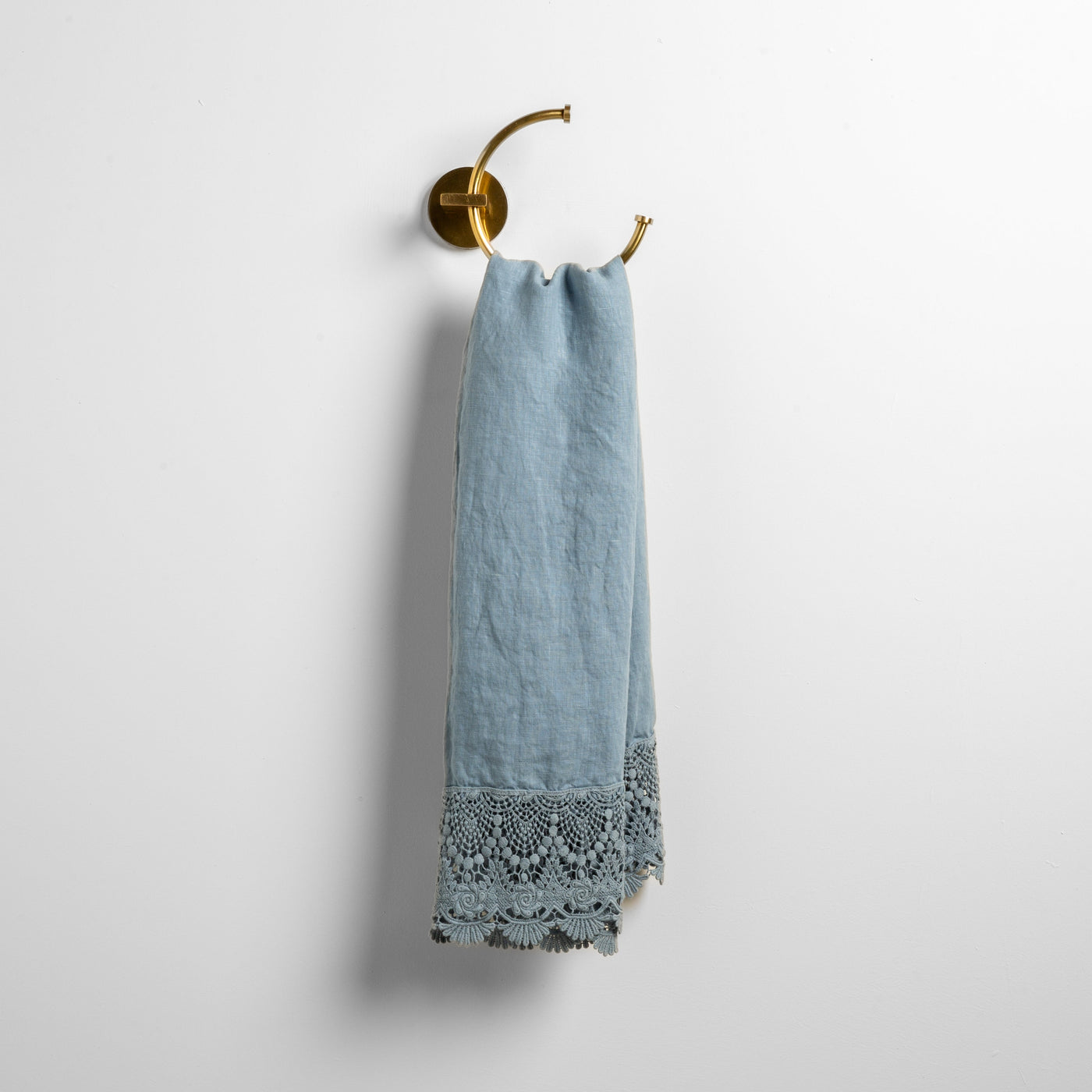 Mattine guest towel in Tahoe Blue, draped on brass ring, showing lace crochet hem detail.