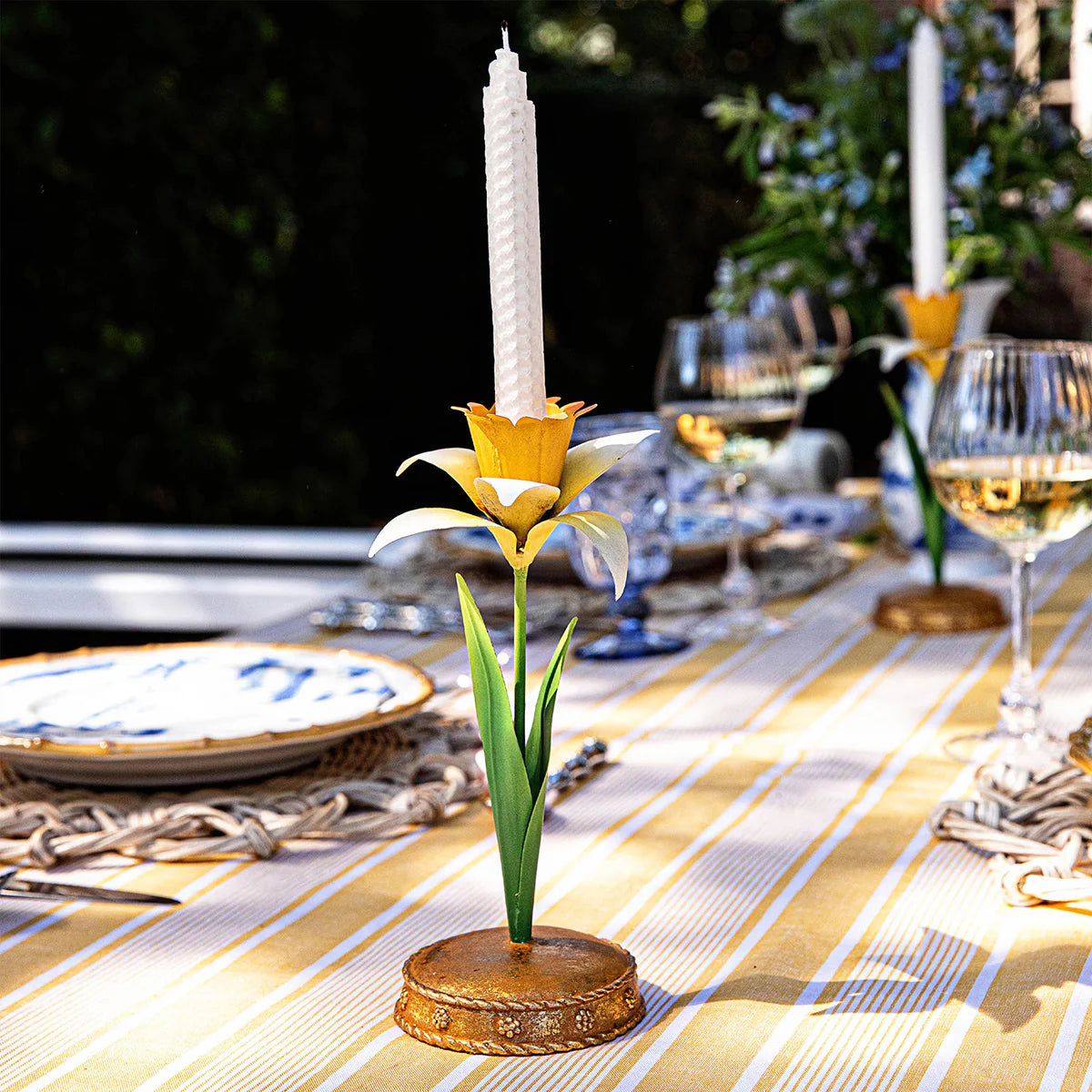 Juliska Meadow Walk candlestick holder styled on striped tablecloth with glassware and blue plates.