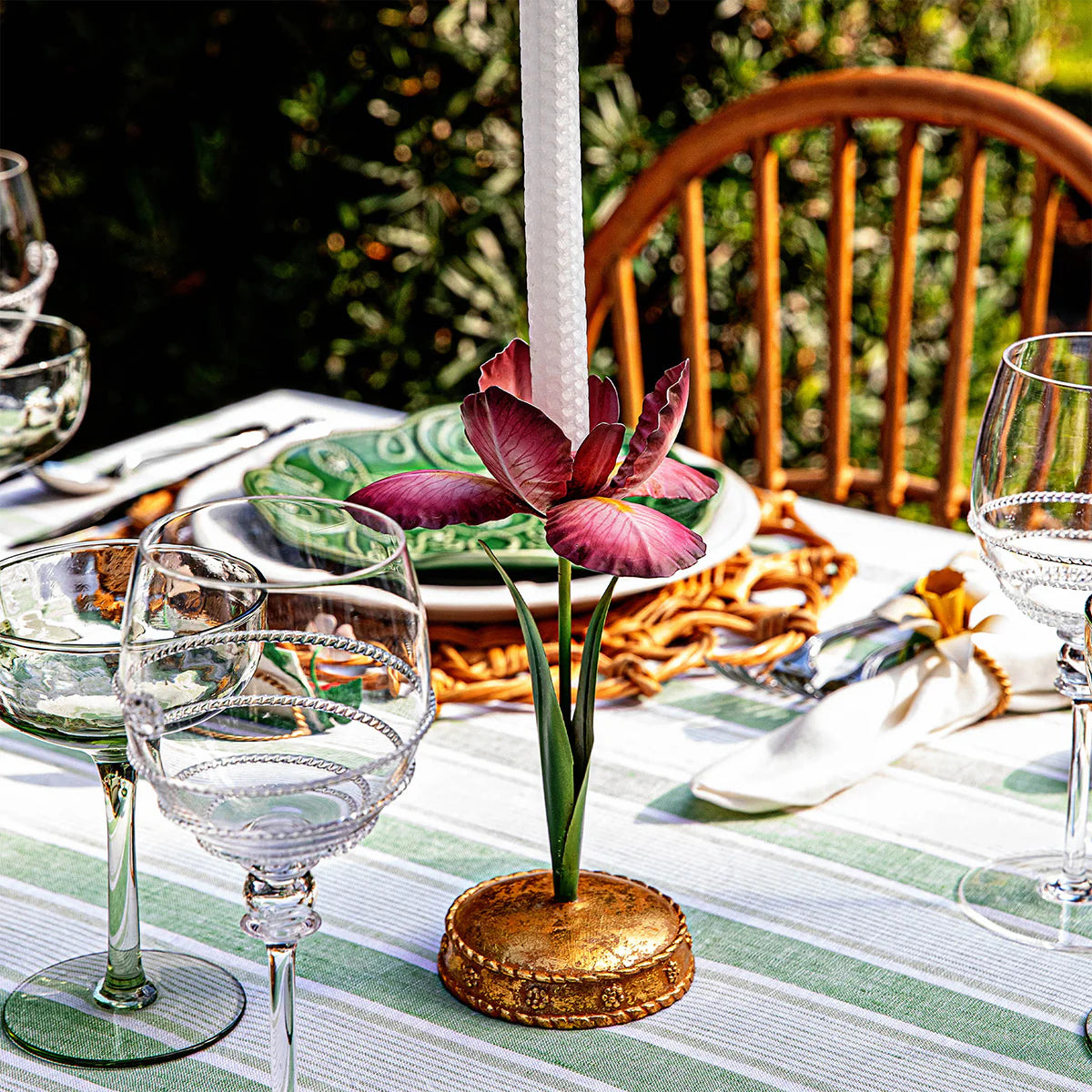 Gilded candlestick holder with burgundy floral motif on a green-striped outdoor tablescape.