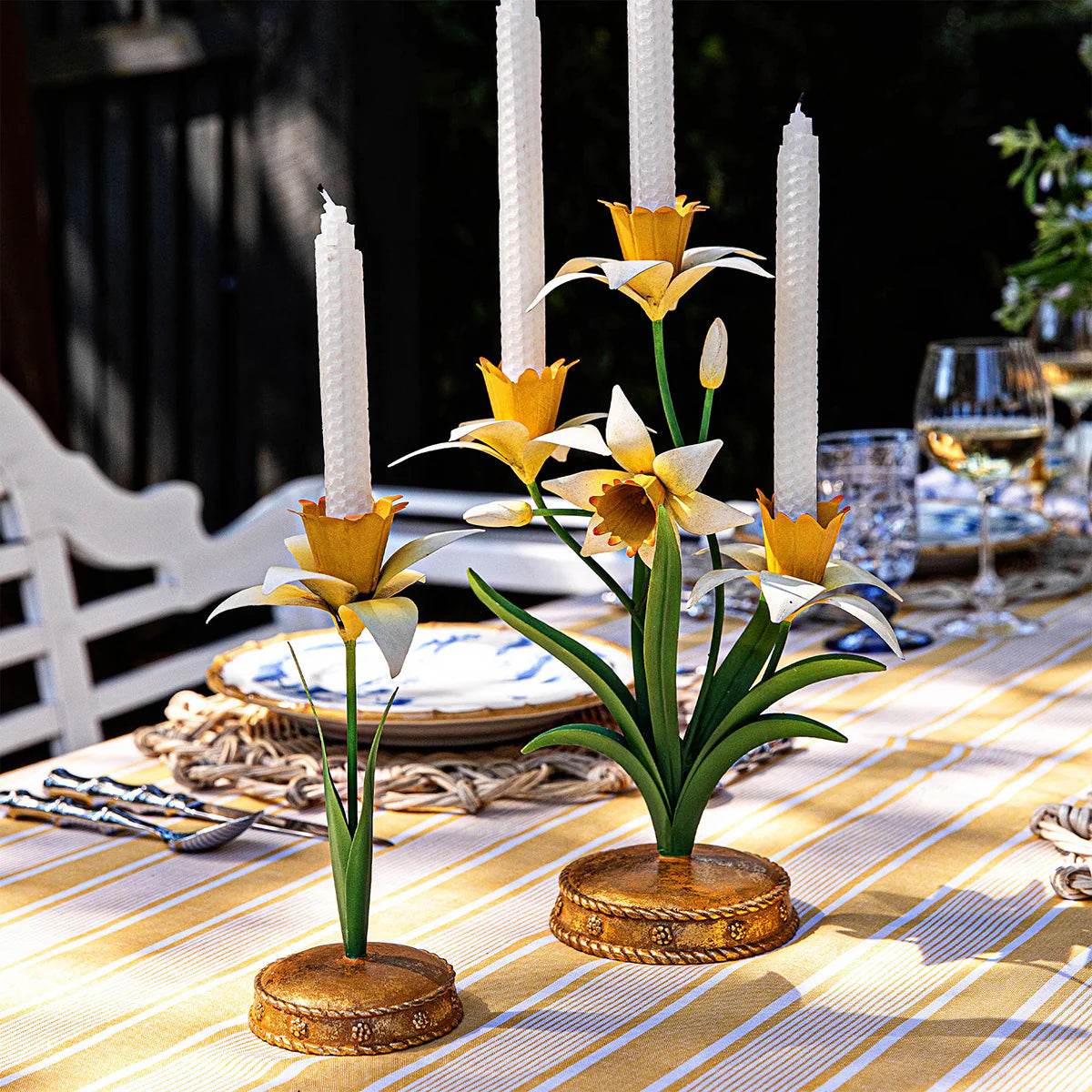 Yellow and white metal daffodil candelabras styled on a striped table with white taper candles.
