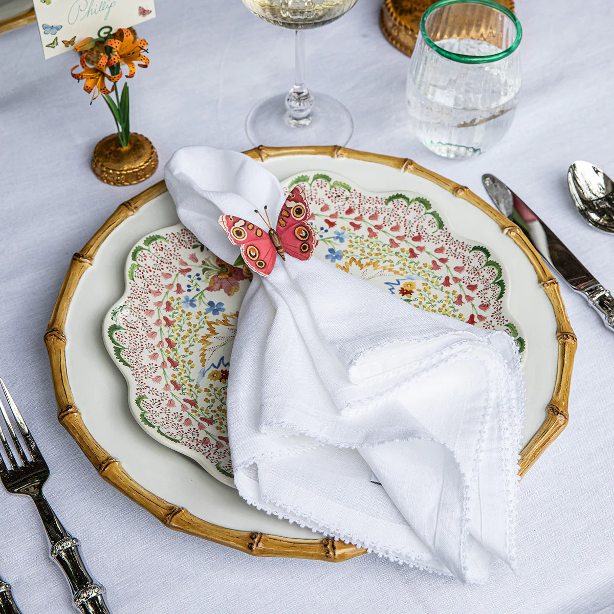 Coral butterfly napkin ring holding white linen napkin on floral-patterned plate.