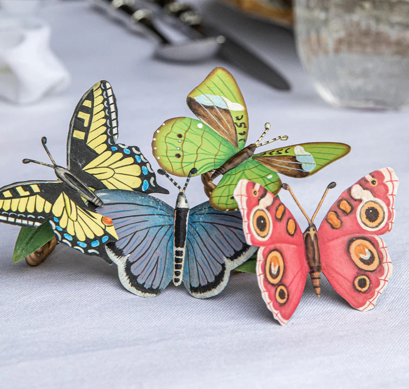 Three Meadow Walk butterfly napkin rings in yellow, blue, and coral on linen.