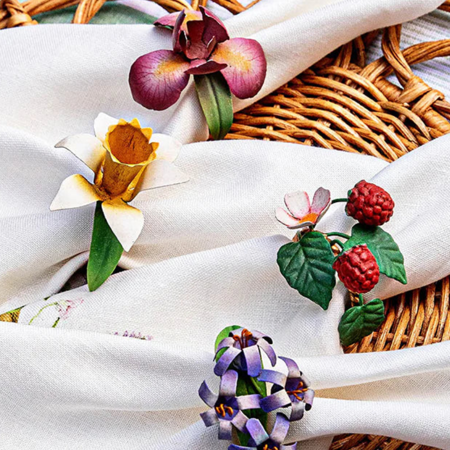 Close-up of four botanical napkin rings with flower and berry motifs on ivory linen napkins.