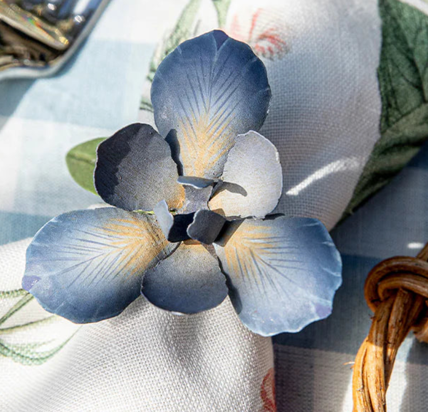 Close-up of steel blue iris flower napkin ring on white linen napkin in sunlight.