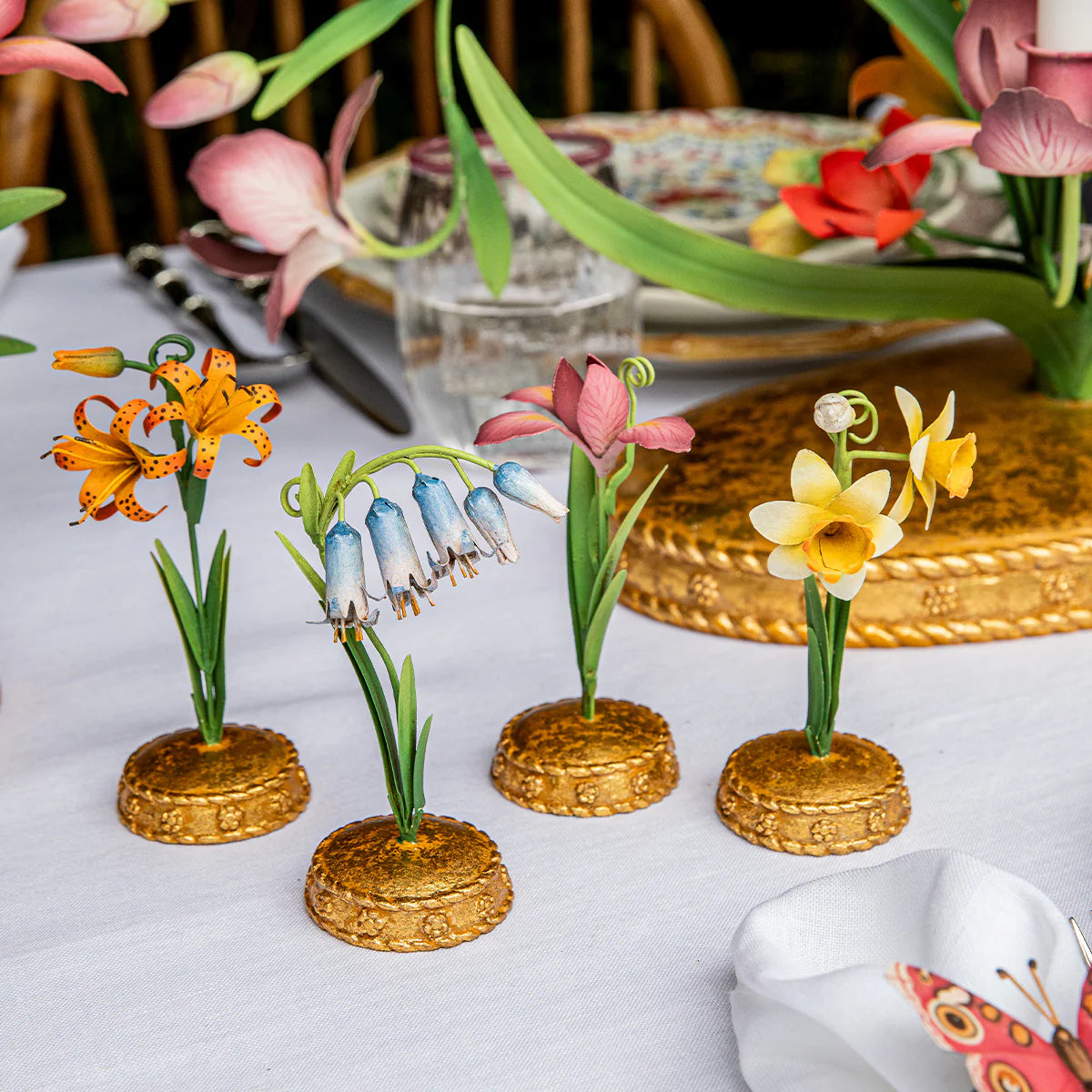 Four Juliska Meadow Walk place card holders with gold bases and botanical flower designs on linen tablecloth.