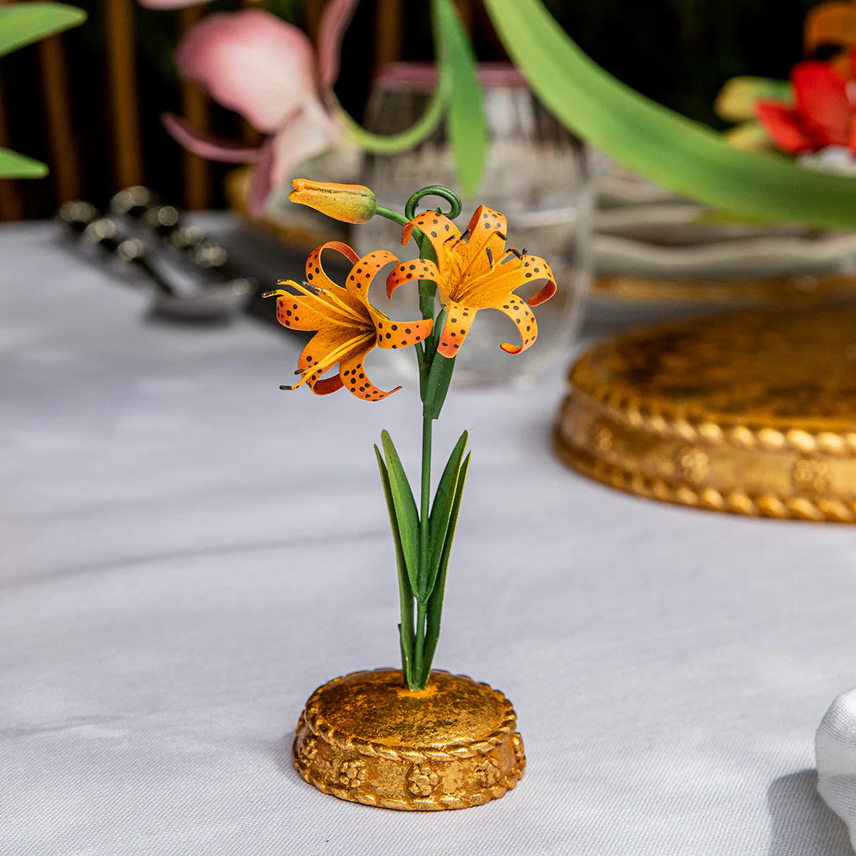 Close-up of orange tiger lily metal place card holder on a gold leafed base.