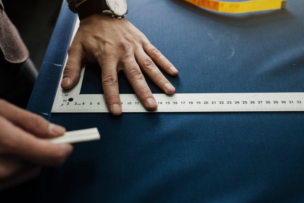 Image of hands holding measuring square and fabric marking chalk on blue fabric