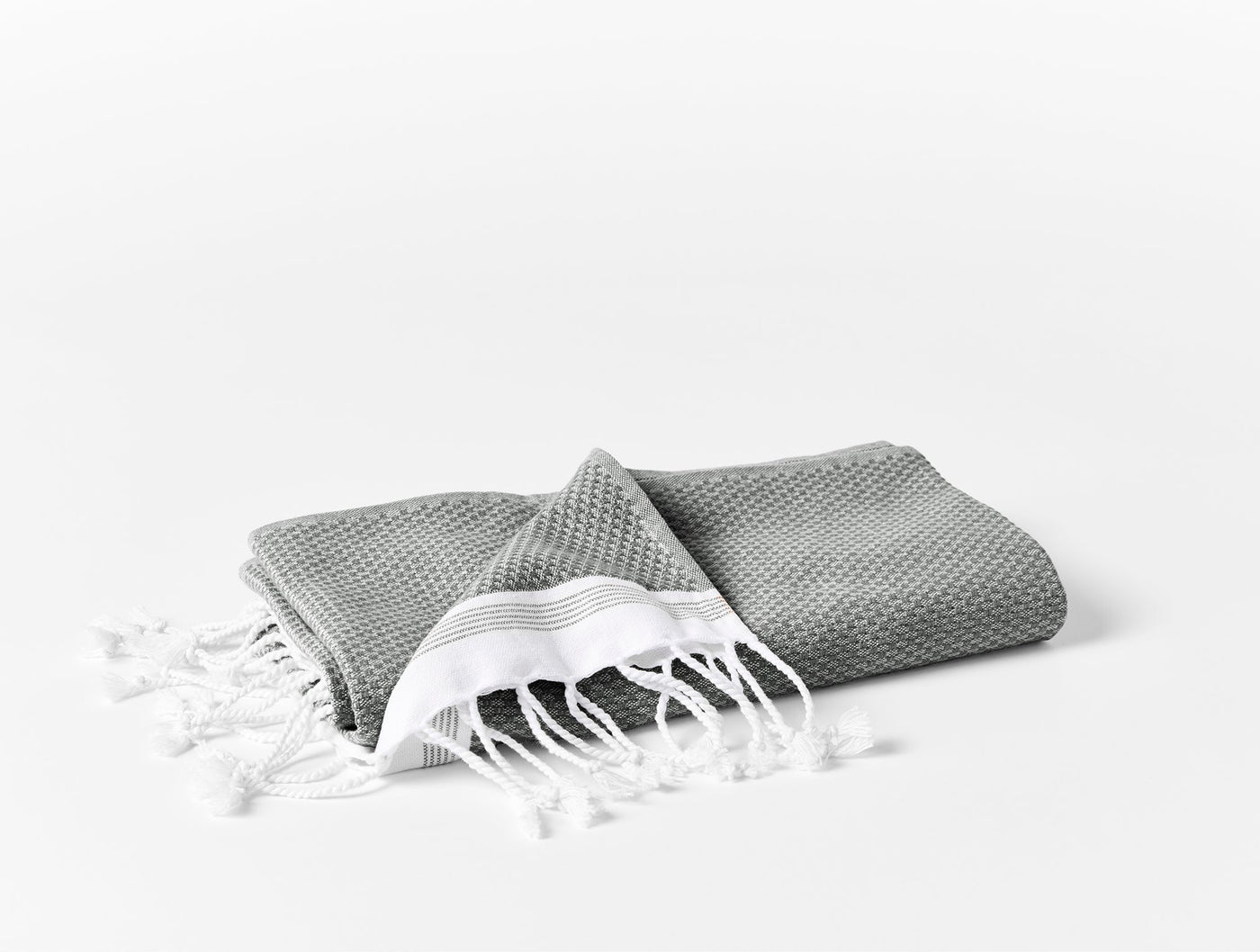 Folded slate grey waffle-weave guest towel with white stripe border and knotted fringe detail.