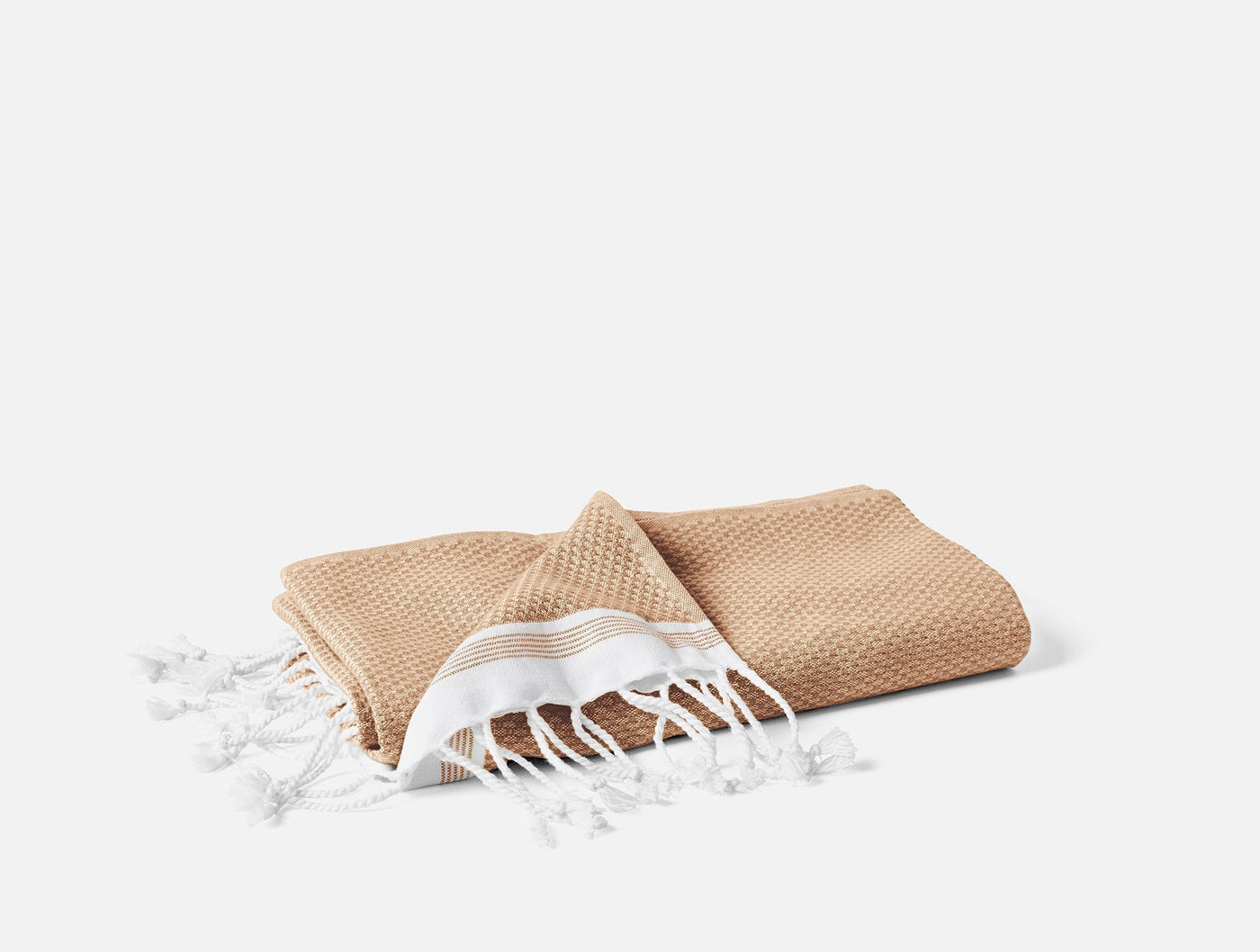 Coyuchi Mediterranean bath towel in camel waffle weave, folded with white fringe detail.