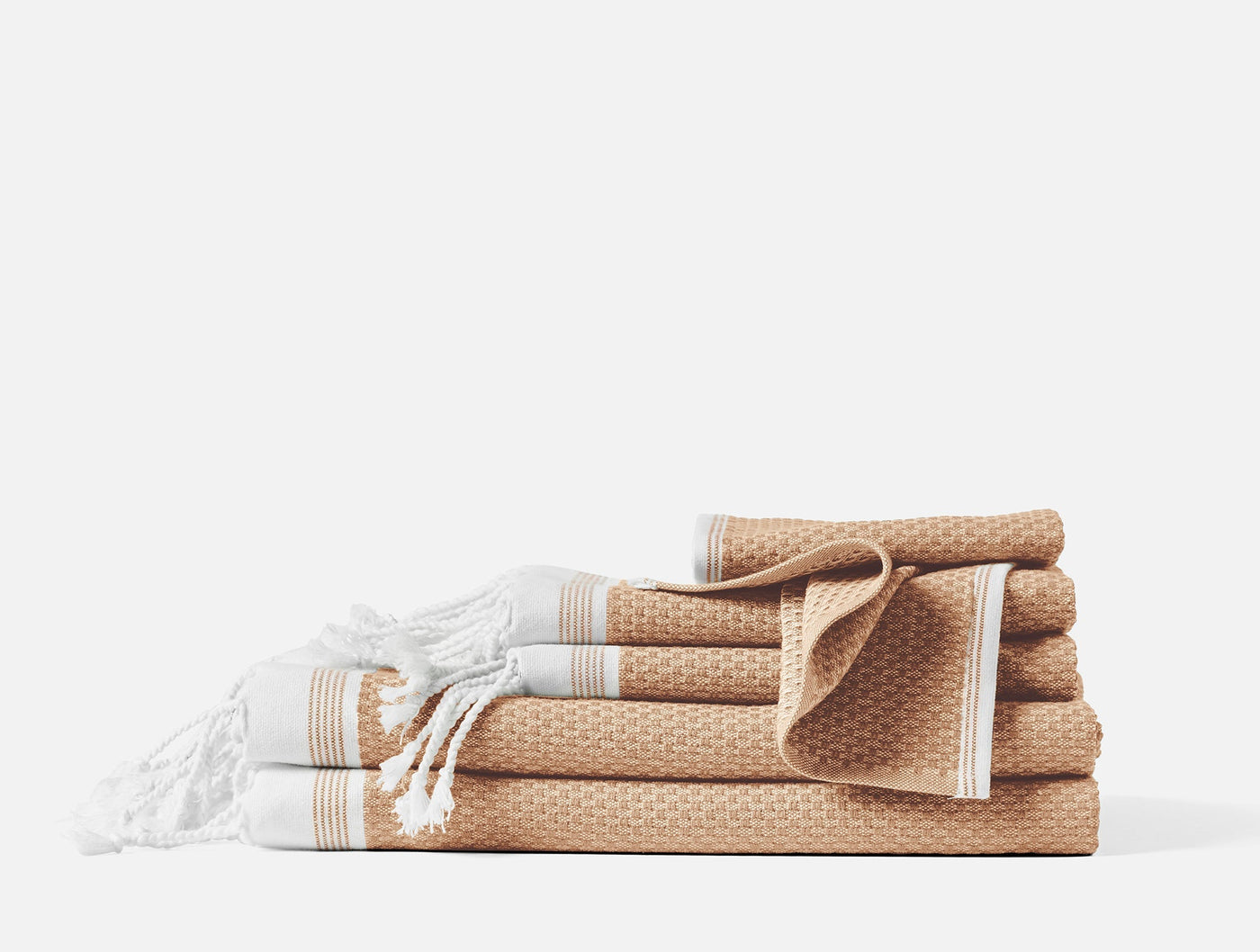 Honey-hued waffle-weave towel set stacked and folded, with fringed hammam towel in front.