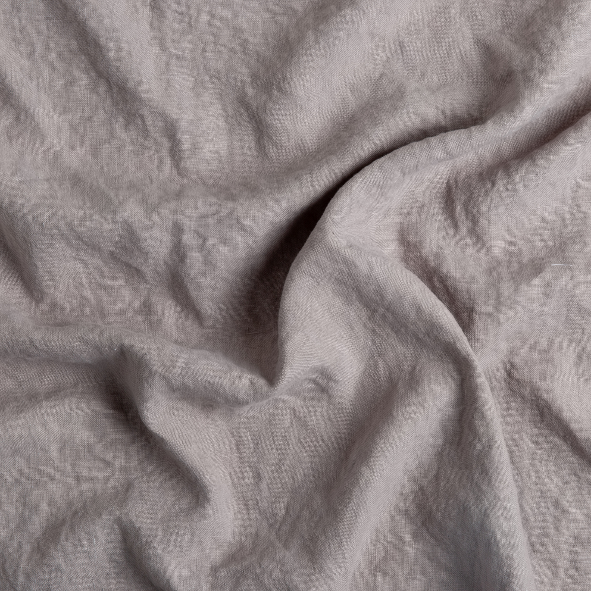 Close-up of softly draped dusty mauve linen fabric showing natural texture and relaxed drape.