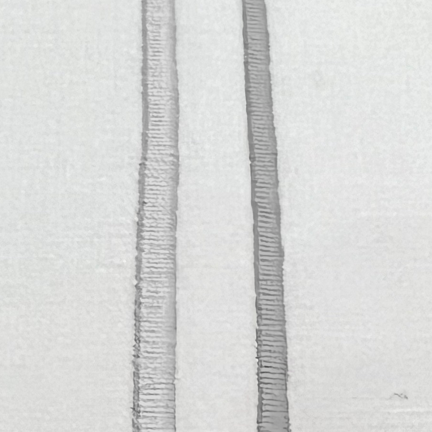 Close-up of two parallel silver embroidered stripes on white linen fabric.