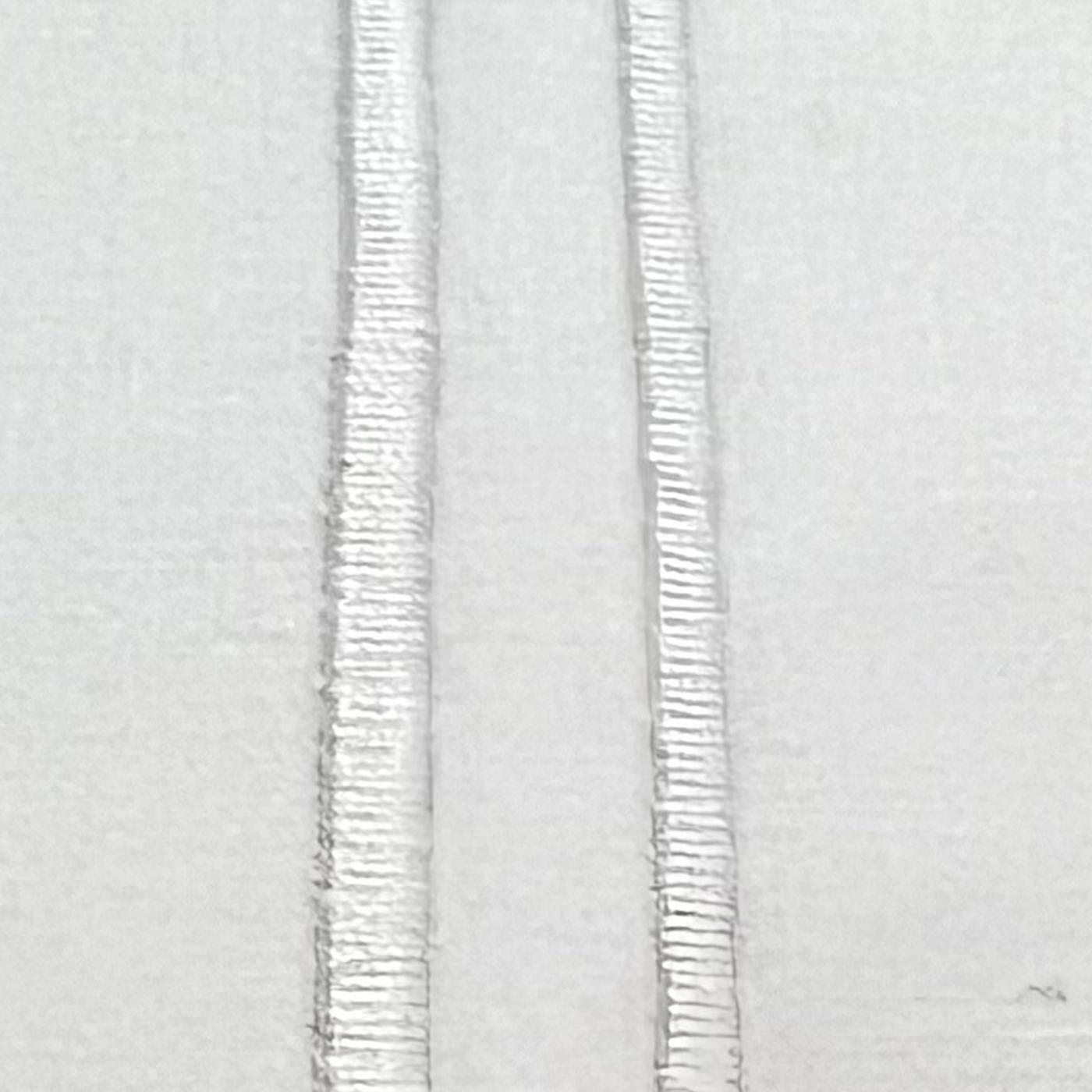Close-up of white-on-white parallel embroidered stripes on cotton sheeting.