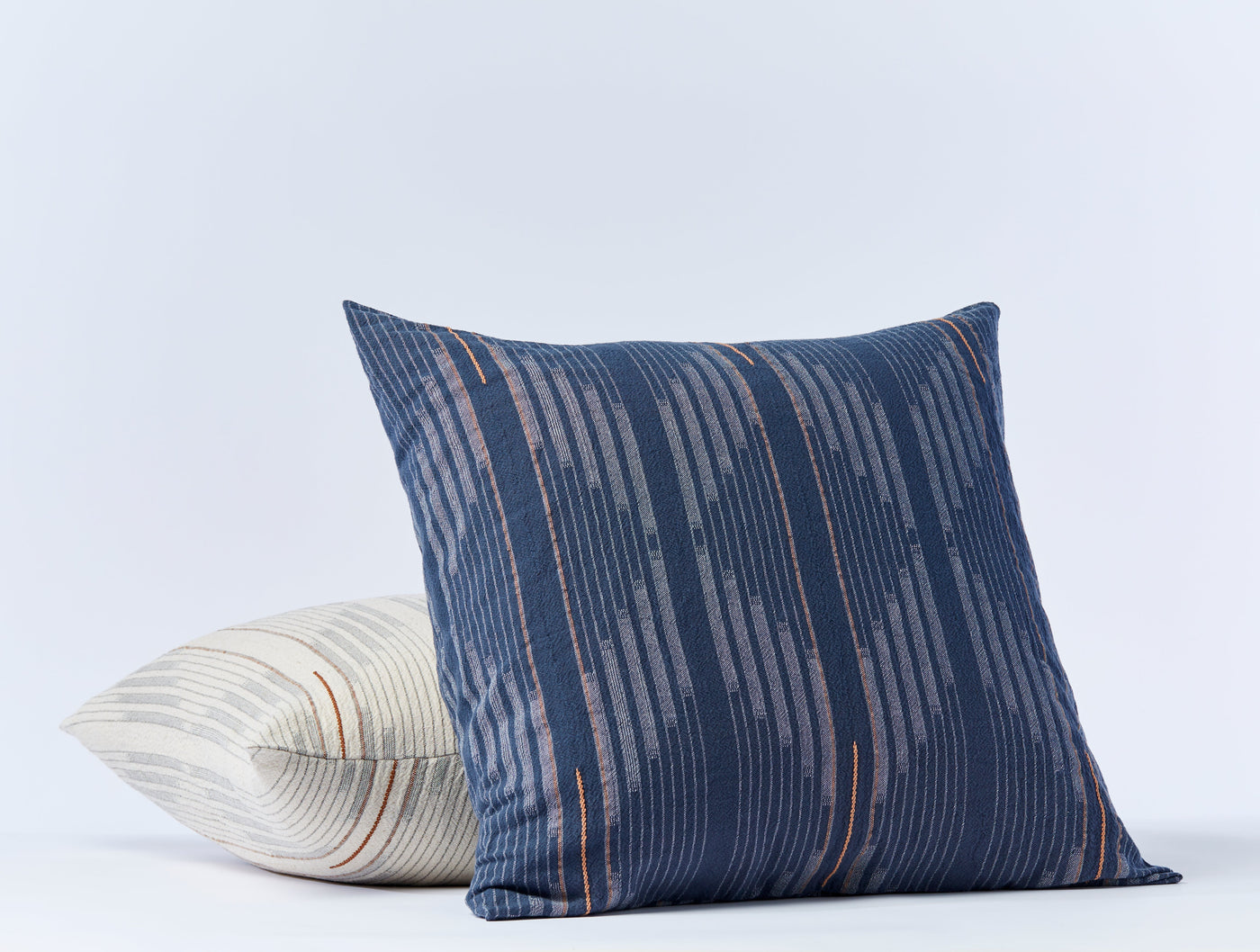 Close-up of navy Coyuchi Morelia sham with copper stripe detail, ivory striped sham beside it.