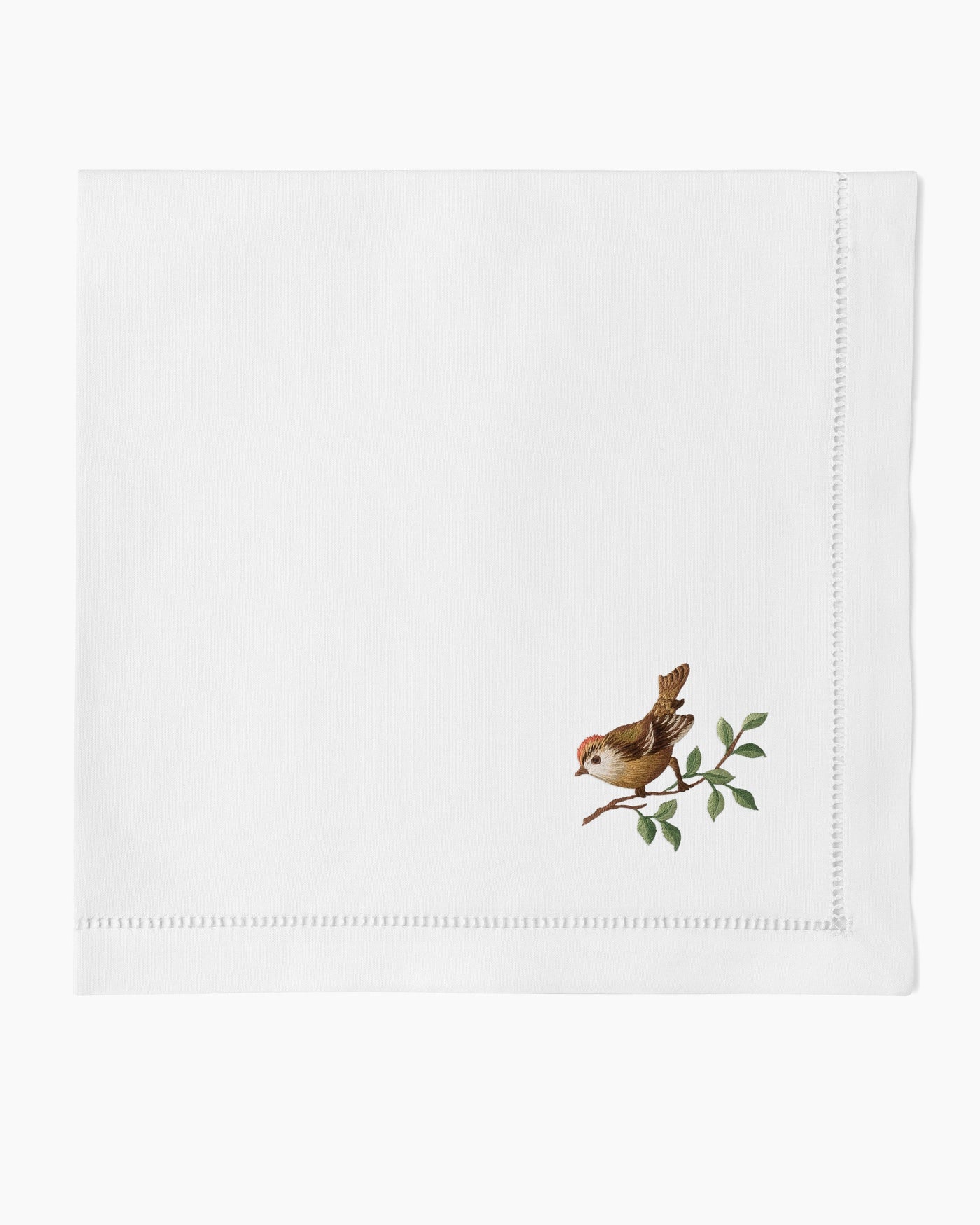 Henry Handwork white linen dinner napkin with embroidered sparrow on green branch.