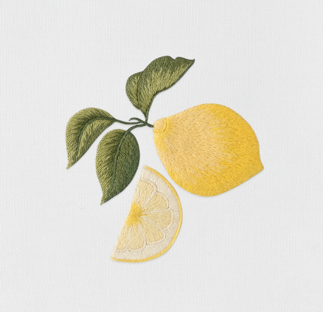 Close-up of embroidered lemon and slice motif with green leaves on ivory linen.