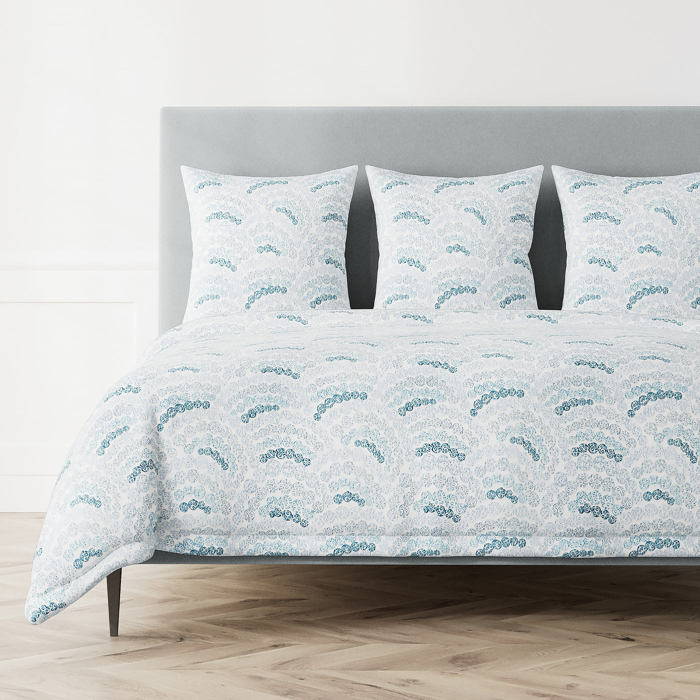Ann Gish Nazar duvet cover in white with teal blue wave and floral pattern, styled on bed.