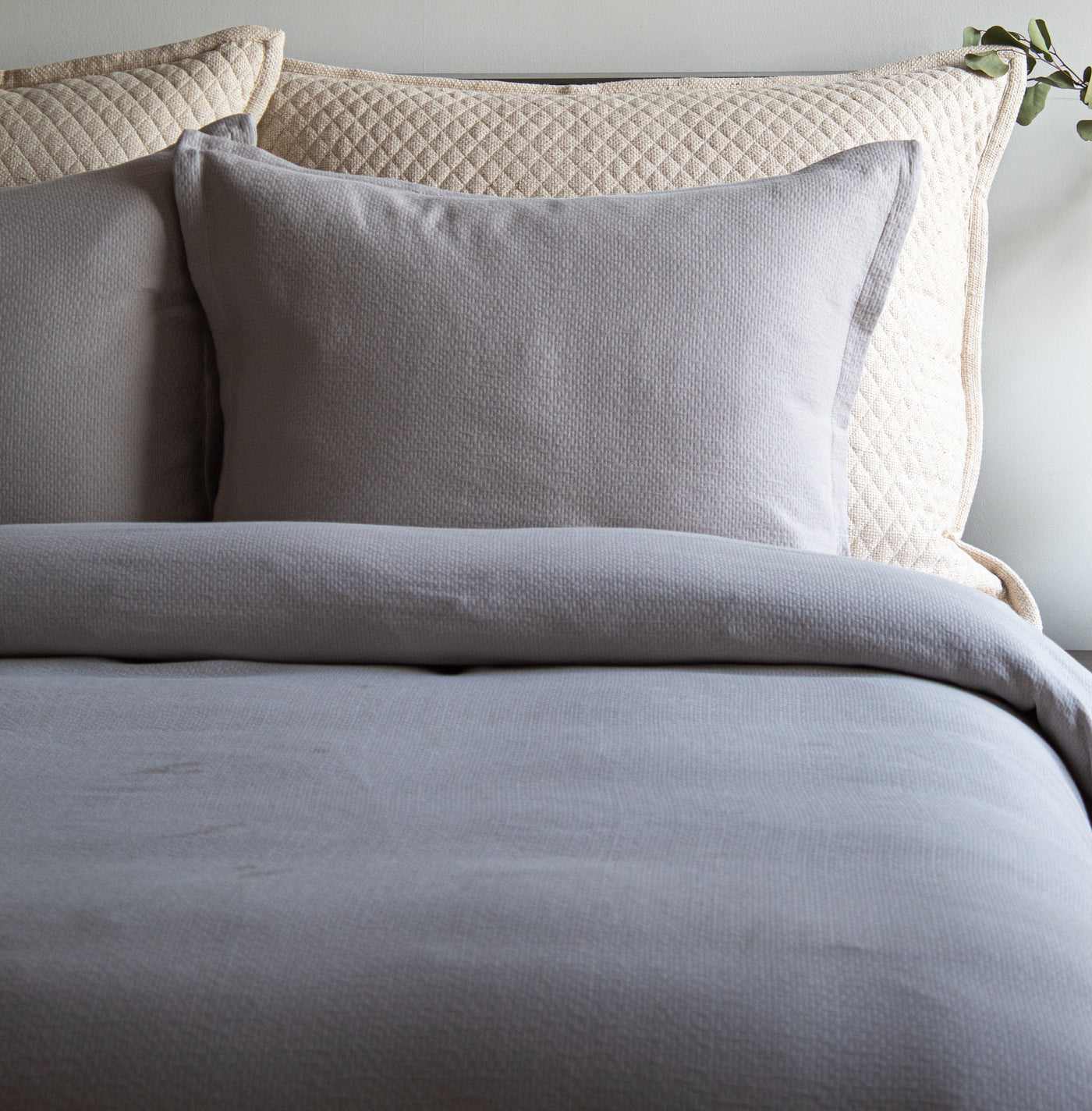 Slate grey textured duvet and sham styled on a bed with a quilted ivory headboard.