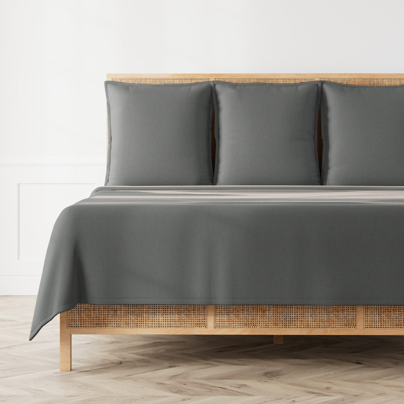 Ann Gish Neo matelasse coverlet set in slate grey, styled on a rattan bed.