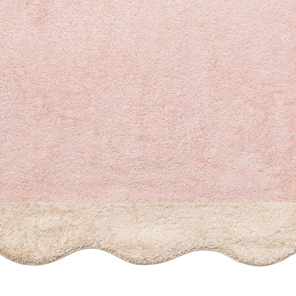 A pink textured rug with a beige scalloped edge at the bottom, inspired by Matouk’s Neptune Pool Towel.