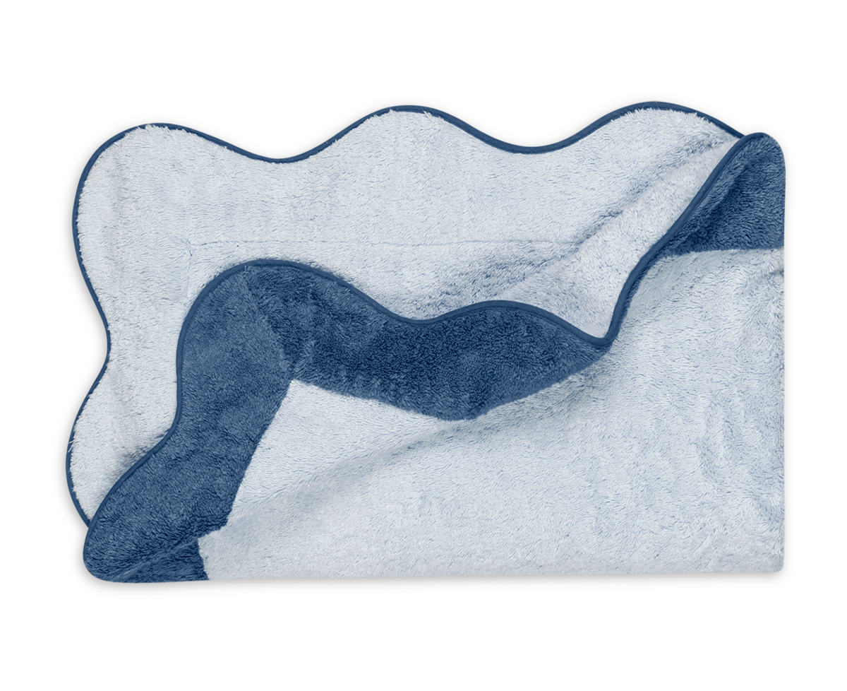 The Neptune Pool Towel by Matouk, in plush light blue Cairo cotton with a wavy dark blue border, is folded with one corner flipped to reveal its soft, absorbent underside.