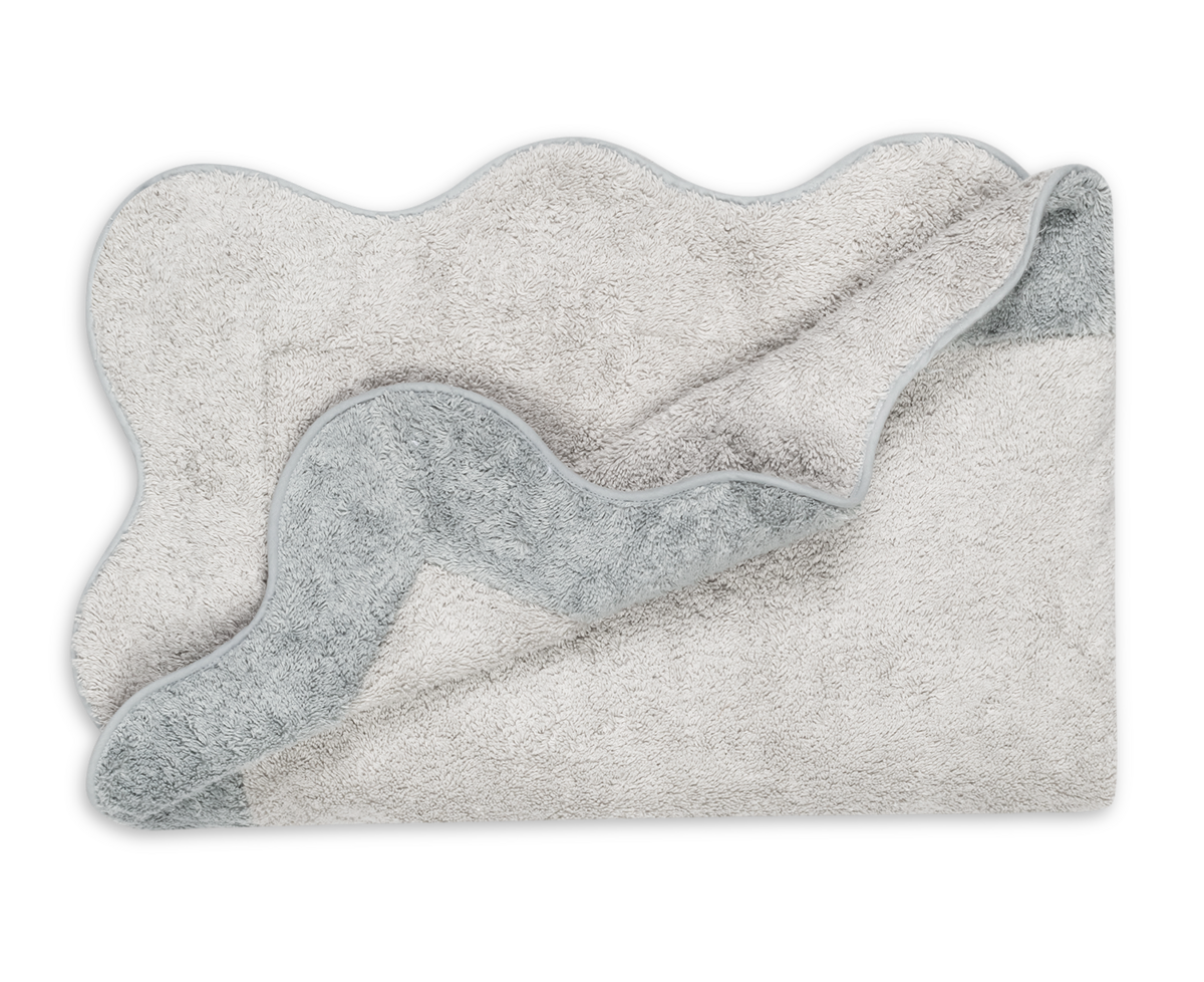 The Neptune | Pool Towel by Matouk is light gray with wavy edges and a textured, absorbent surface, shown partially folded to display both sides against a white background.