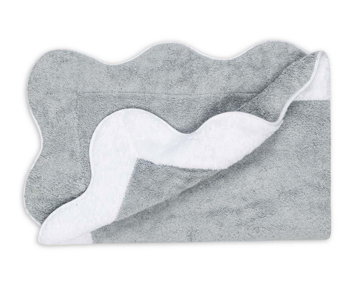 The Matouk Neptune | Pool Towel in gray, featuring a scalloped edge and absorbent towel material, is partially folded to reveal its white underside against a plain background.