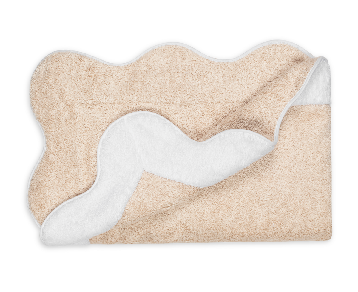 The Matouk Neptune | Pool Towel features tan and white wavy edges. Shown laid flat, one corner is folded to reveal its white underside.