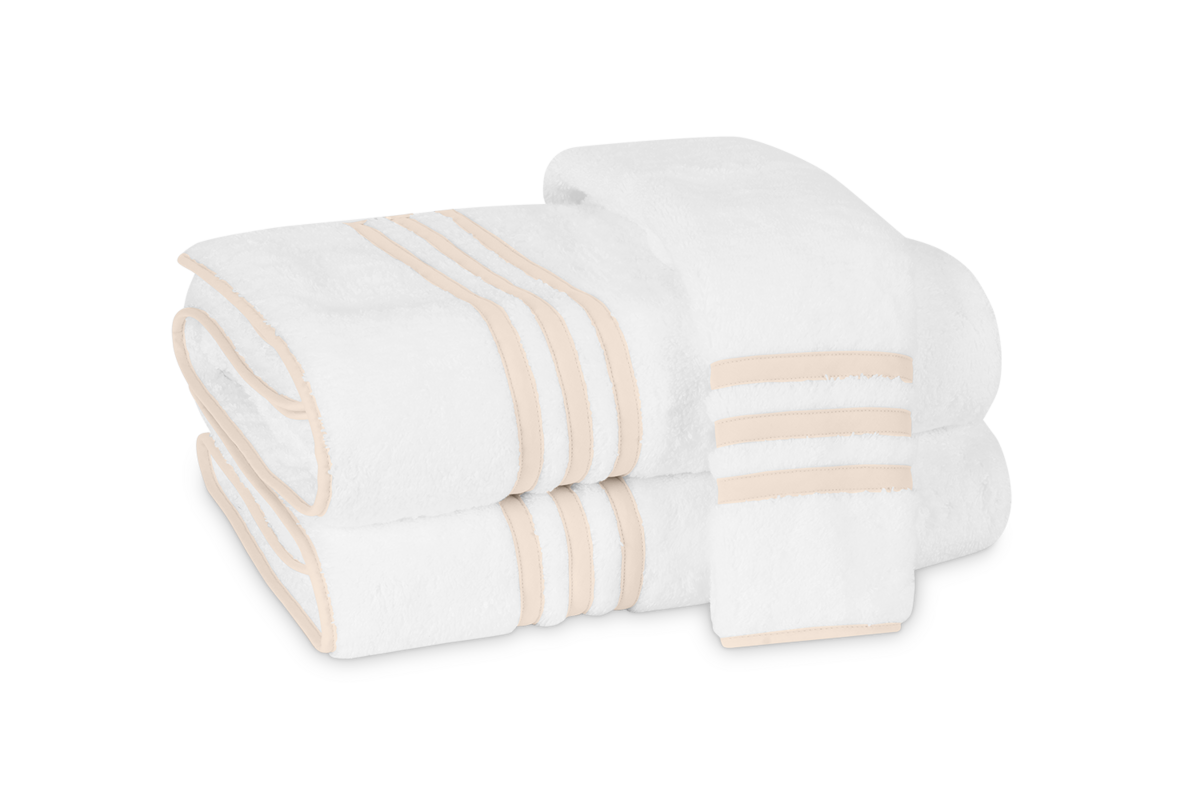 Three folded Newport Bath Towels by Matouk, made from white Cairo cotton terry with beige stripes and an appliqué-tape border, are stacked against a plain white background.