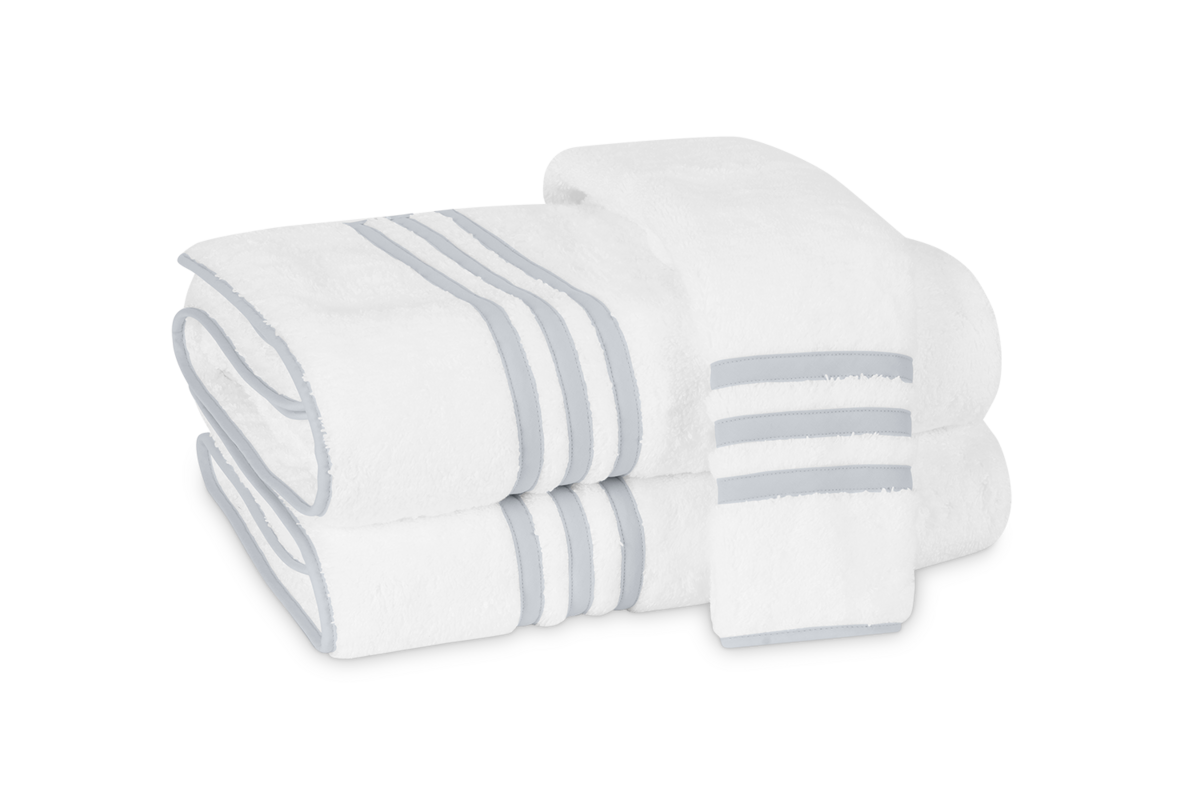 Three neatly folded Matouk Newport hand towels in white, featuring gray stripes and an appliqué-tape border, are stacked on a white background.