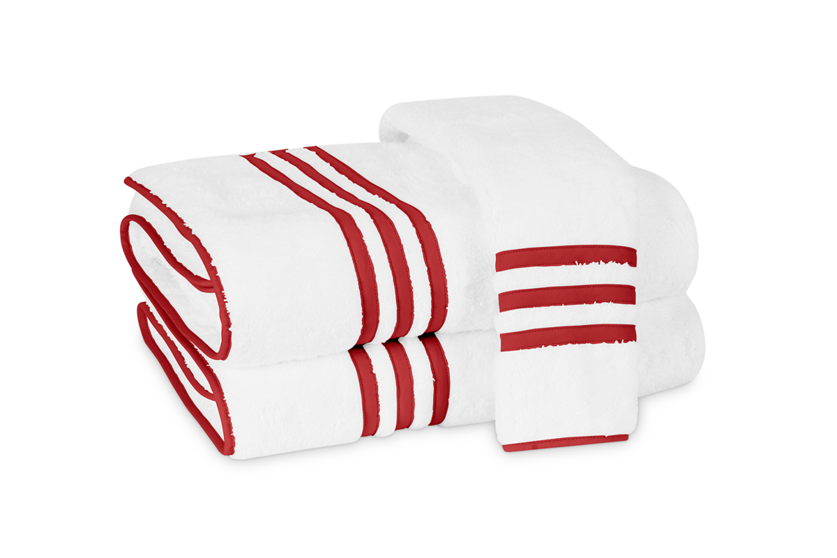 The Matouk Newport Guest Towel features three parallel red stripes on a white background with an appliqué-tape border, neatly folded and stacked for a classic, elegant look.