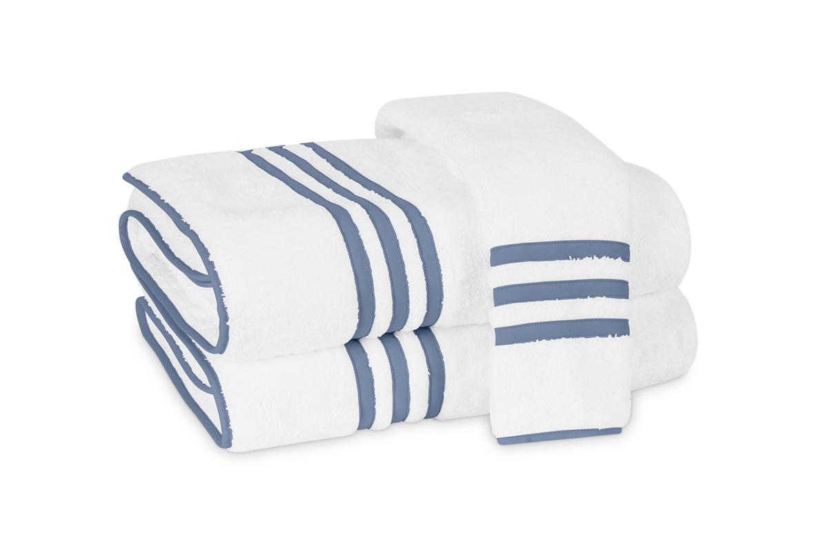 Two white Newport hand towels by Matouk, featuring three horizontal blue stripes and an appliqué-tape border, are neatly folded with one draped on top.