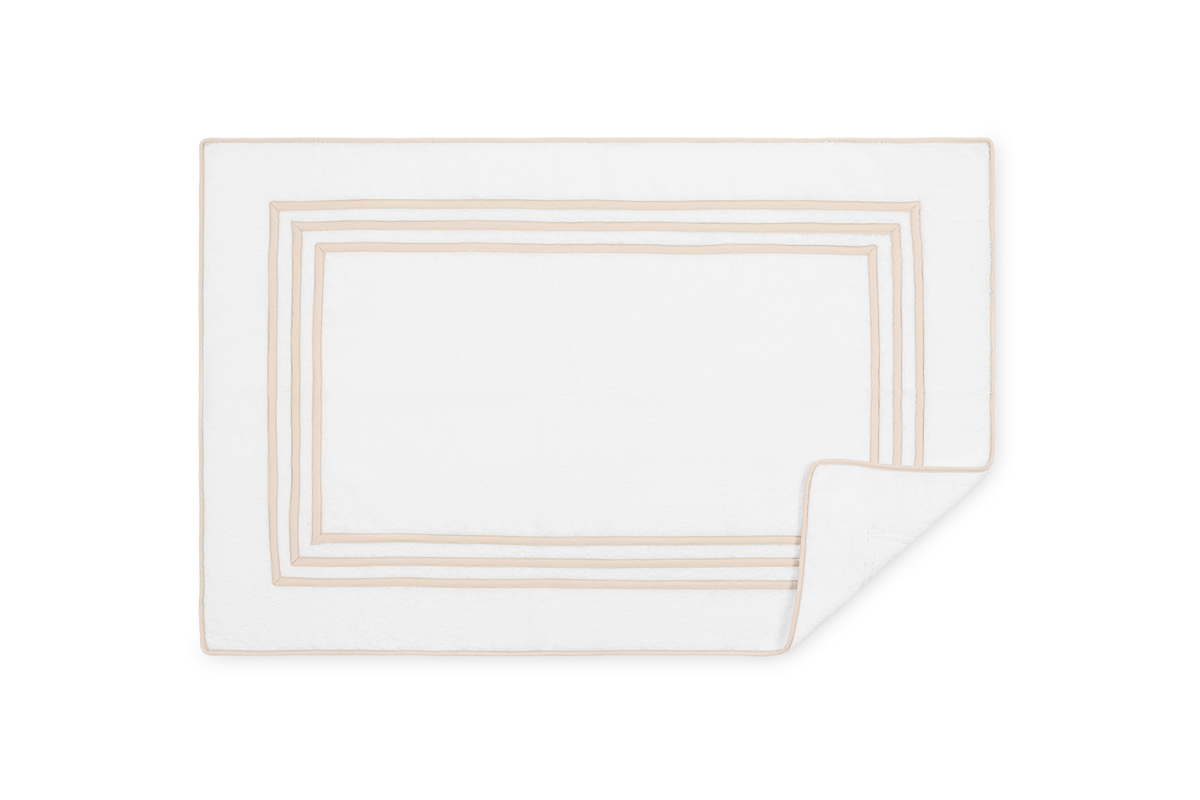 Matouk Newport white tub mat with champagne triple-stripe border, corner folded.
