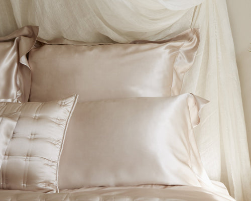 Champagne silk pillow sham with satin border, layered atop tufted bedding.