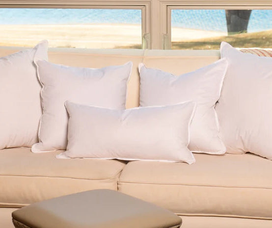 Beige sofa with white pillows in a room with red chairs and a window view.