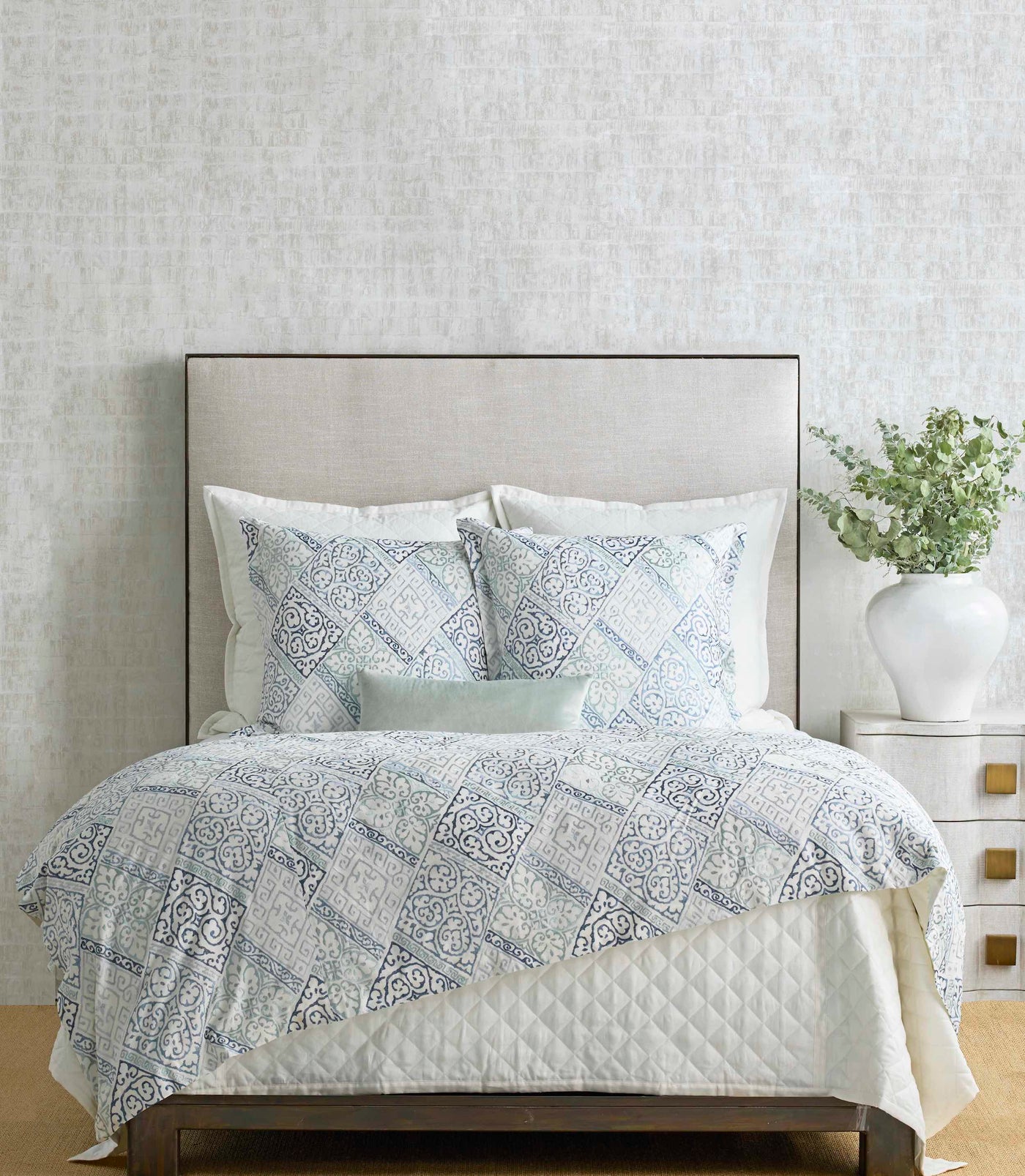 Duvet and shams with blue diamond medallion print styled on a bed with a mint accent pillow.