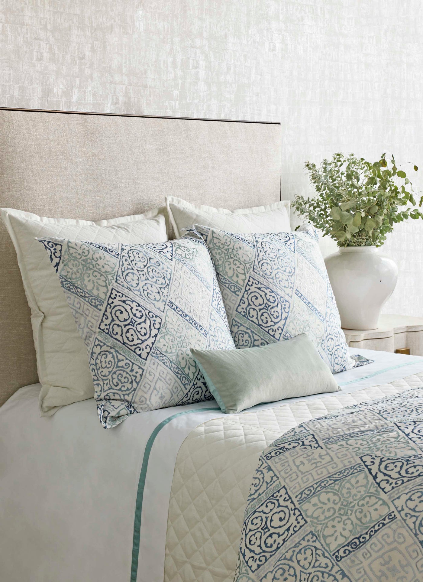 Quilted duvet and decorative pillows in ivory with blue medallion print, styled on a neutral bed.