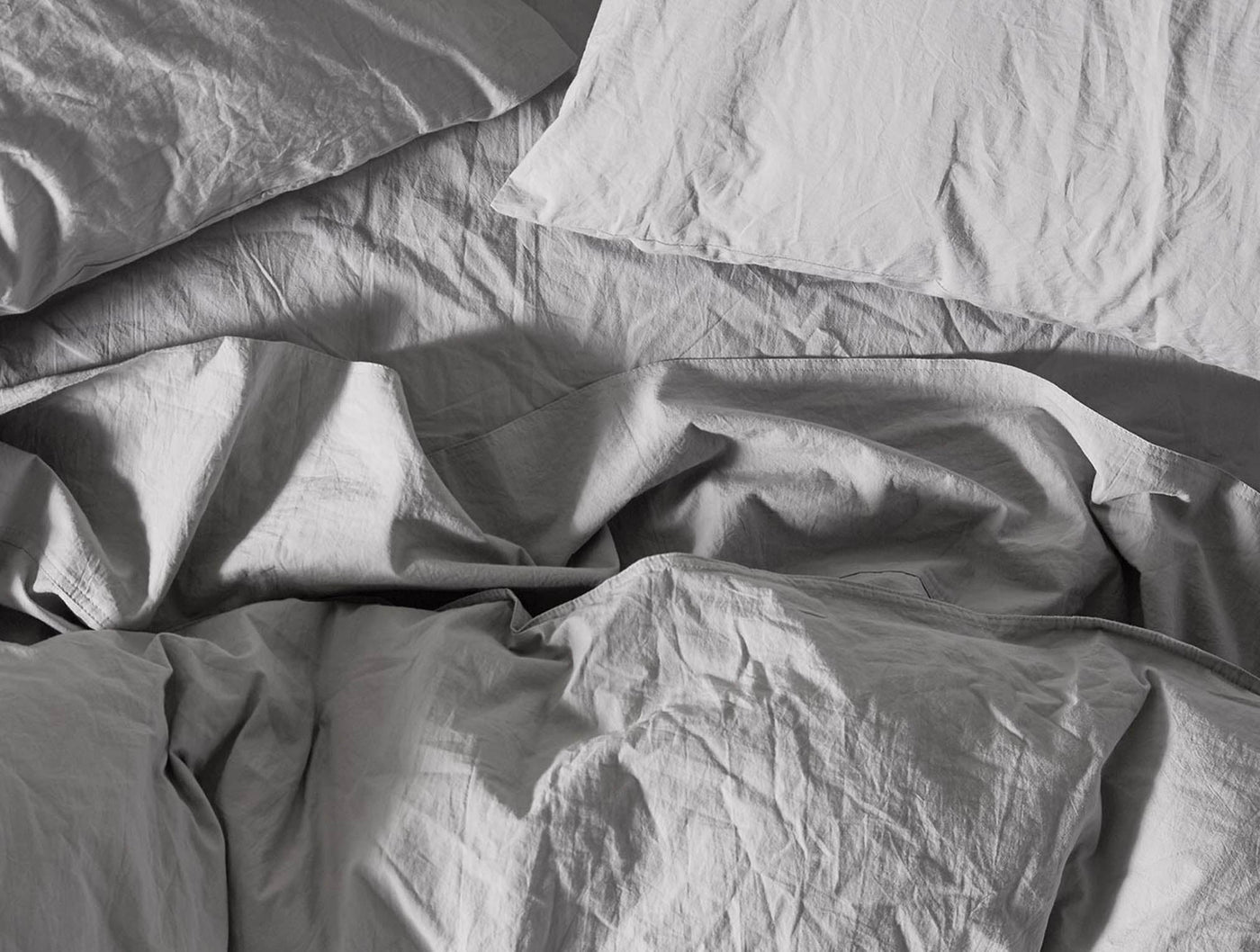 Rumpled silver grey percale sheets with natural crinkle texture, soft dramatic shadows.